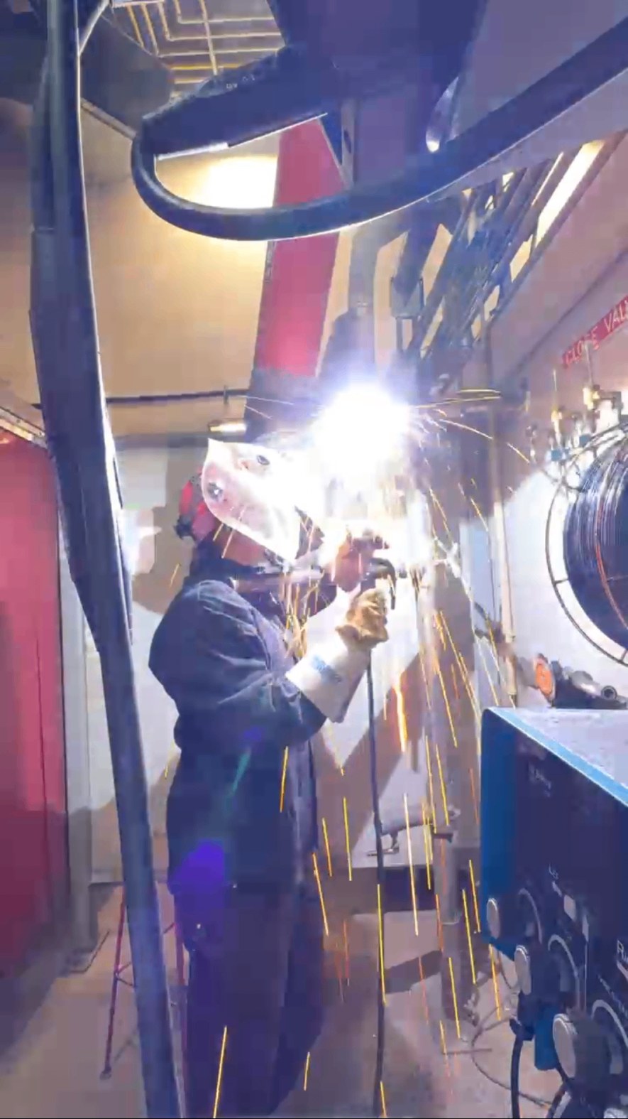 Welder in protective gear working with sparks flying in a training shop